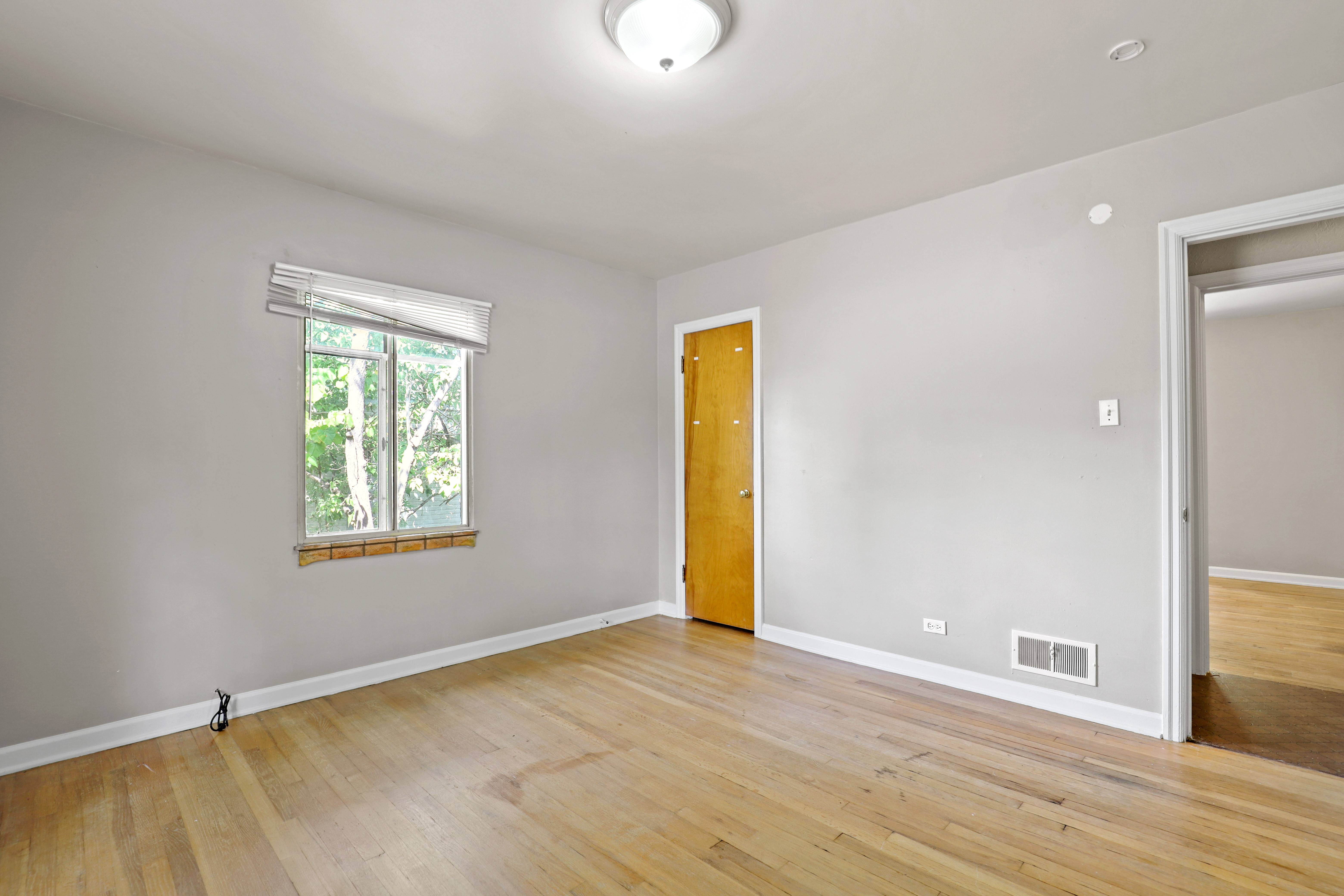 an empty living room with wood floors and a door to a bedroom